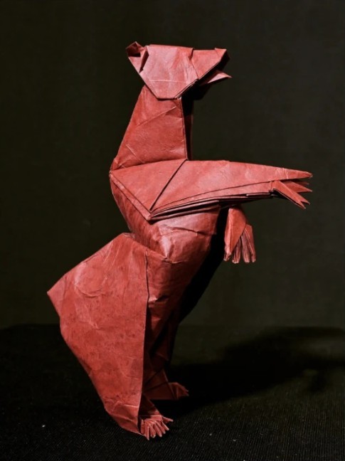 Origami bear folded from red paper, standing on its hind legs