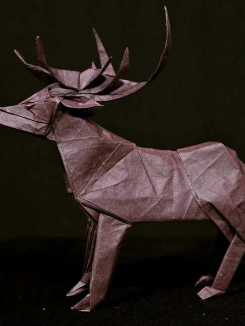 Origami stag folded from brown paper, shown against a dark backdrop